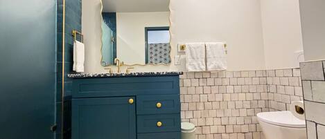 Une salle de bain avec un meuble-lavabo bleu foncé, des toilettes blanches et un miroir surmonté de luminaires.