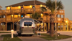 A large, multi-story wooden building with balconies, a parked trailer, and a palm tree. - The Breeze Beachfront Resort (Surfside Beach)