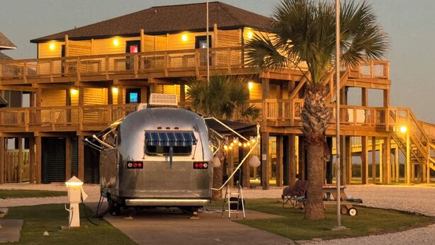 A large, multi-story wooden building with balconies, a parked trailer, and a palm tree. - The Breeze Beachfront Resort (Surfside Beach)
