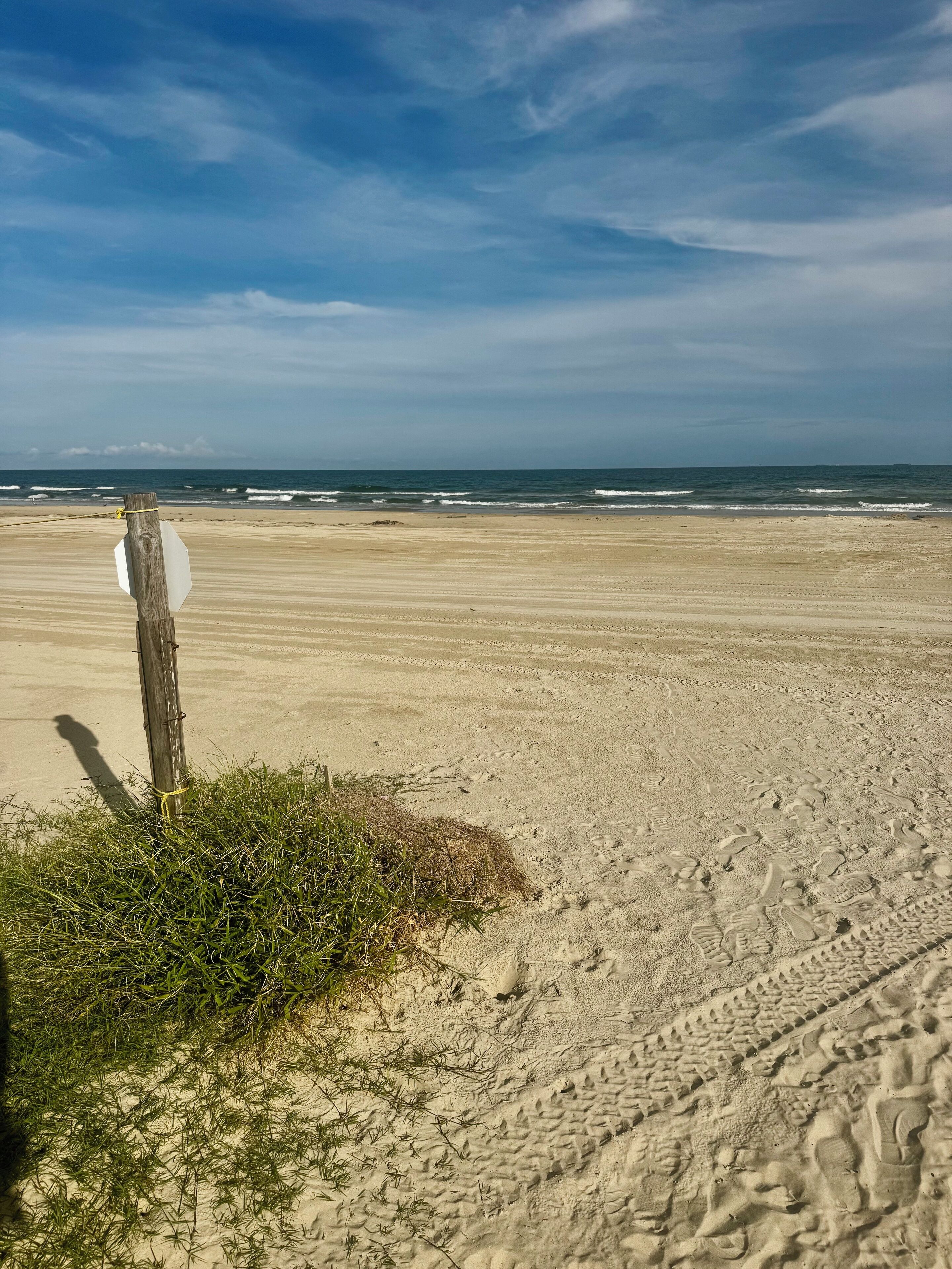 A sandy beach with footprints and a wooden post with a sign.
