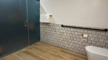 Un baño moderno con piso de madera, inodoro blanco, toallero y zona de ducha con pared de azulejos azul oscuro.