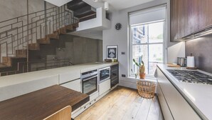 Una cocina moderna con una escalera de madera, hornos empotrados, un ventanal grande y una cesta de mimbre.