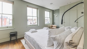 Un dormitorio moderno con una cama grande, dos ventanas, una silla y un armario.