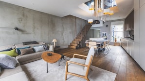 Una sala de estar moderna con sofá, mesa de centro y sillones, una escalera que lleva a una cocina y un comedor.