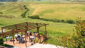 Een terras met buitenmeubelen, omringd door een houten pergola, met uitzicht op een glooiend landschap.
