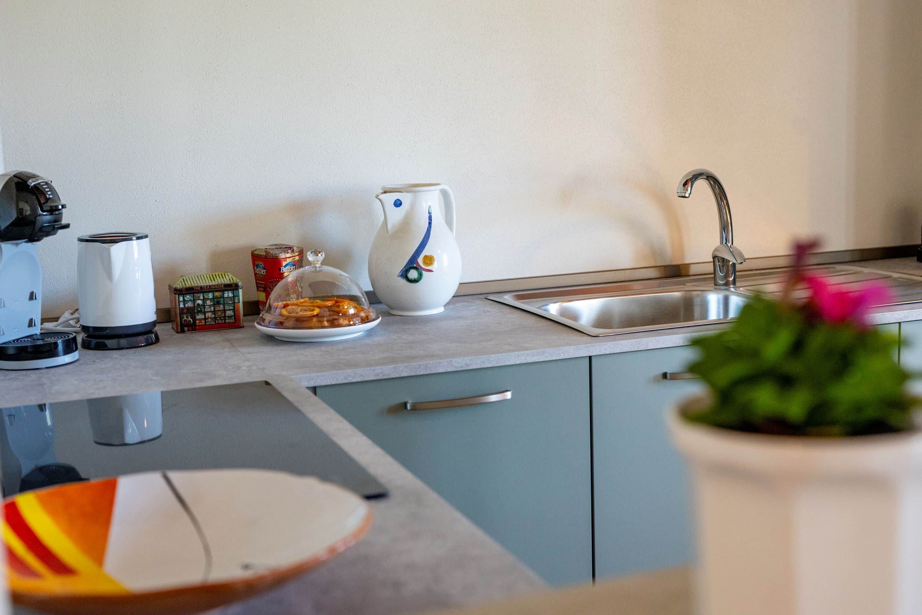 Een keuken met een spoelbak, waterkoker, broodrooster en koffiezetapparaat op het aanrecht.