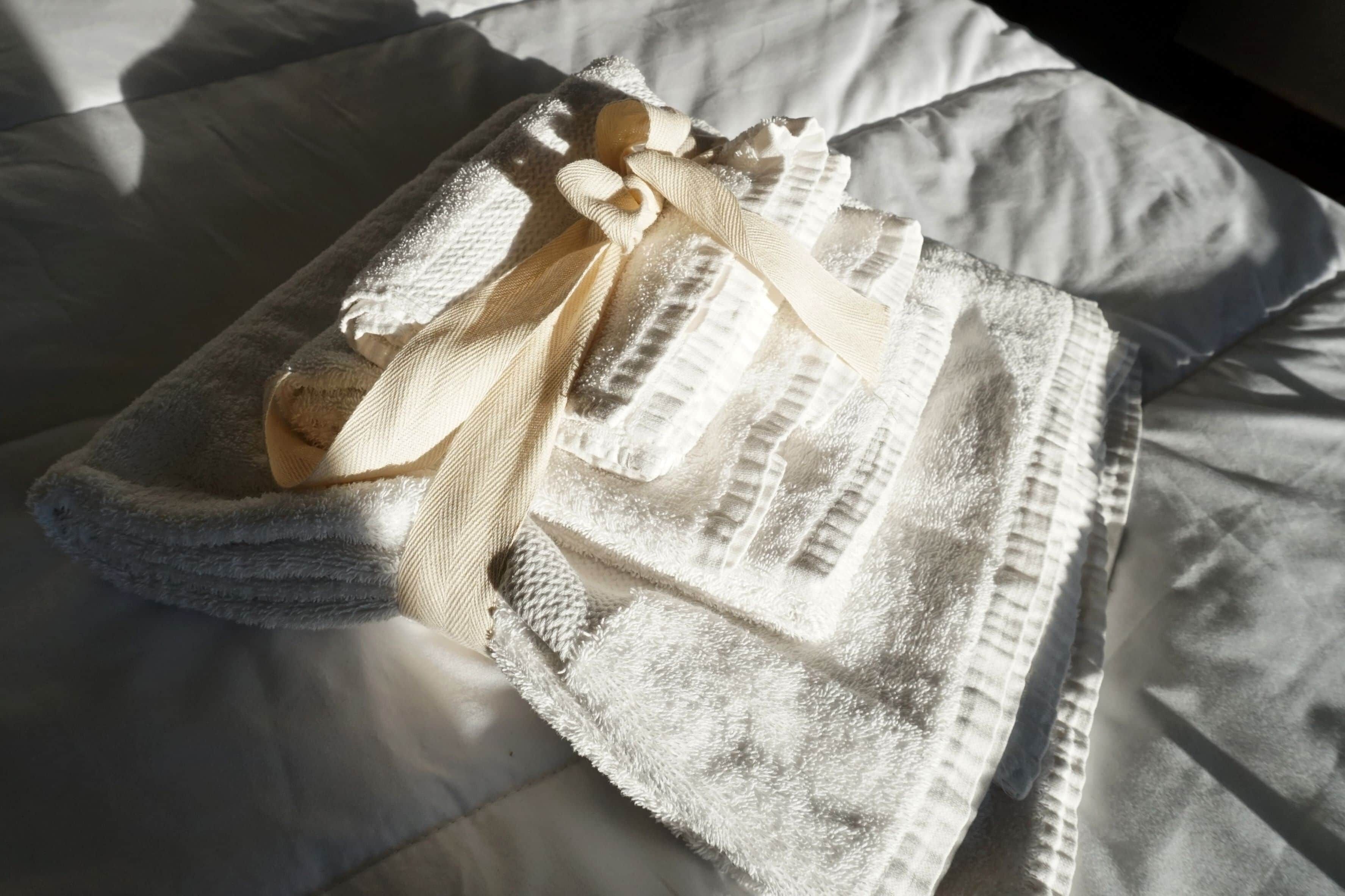 A neatly folded towel with a bow on a bed.