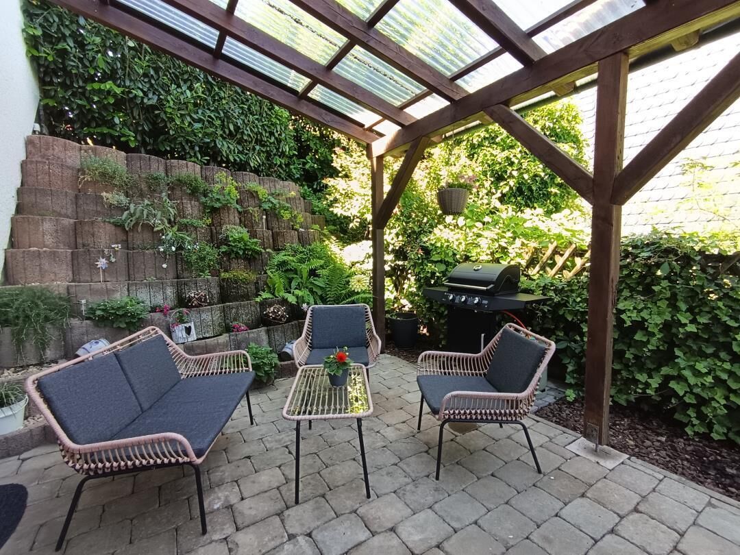 Eine Terrasse im Freien mit Korbmöbeln, einem Grill und einem gläsernen Anbau.