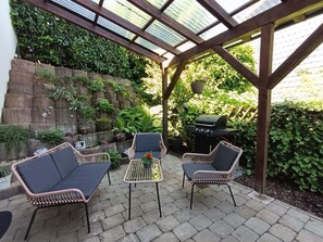 An outdoor patio with wicker furniture, a grill, and a glass-enclosed structure.