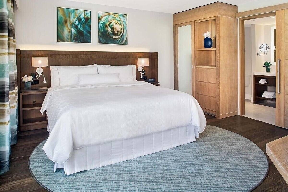 A hotel room with a large bed, two bedside tables with lamps, a wooden wardrobe, and a bathroom visible through an open door.