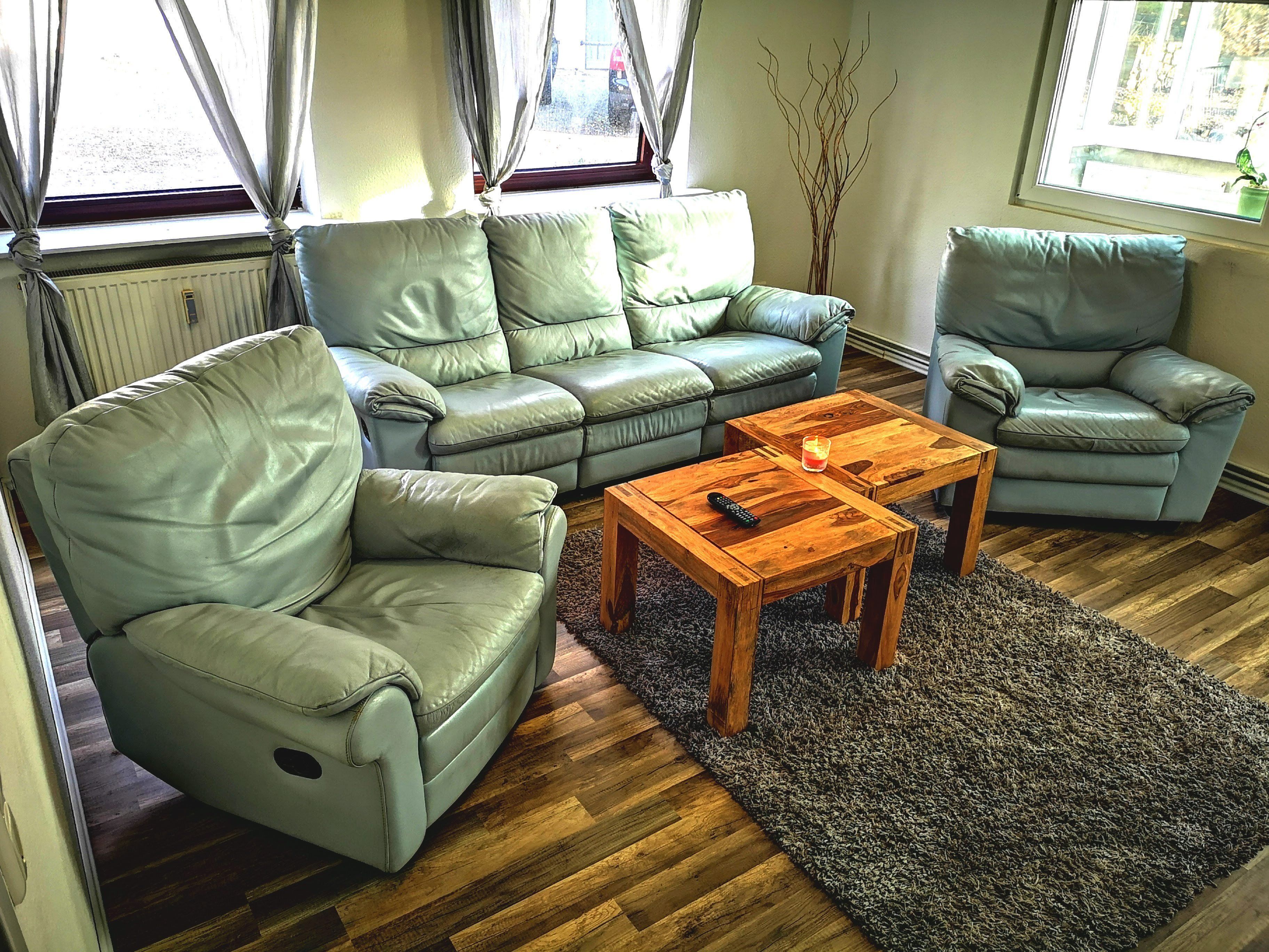Un salon comprenant un canapé d’angle, deux fauteuils, une table basse et une fenêtre avec des rideaux.