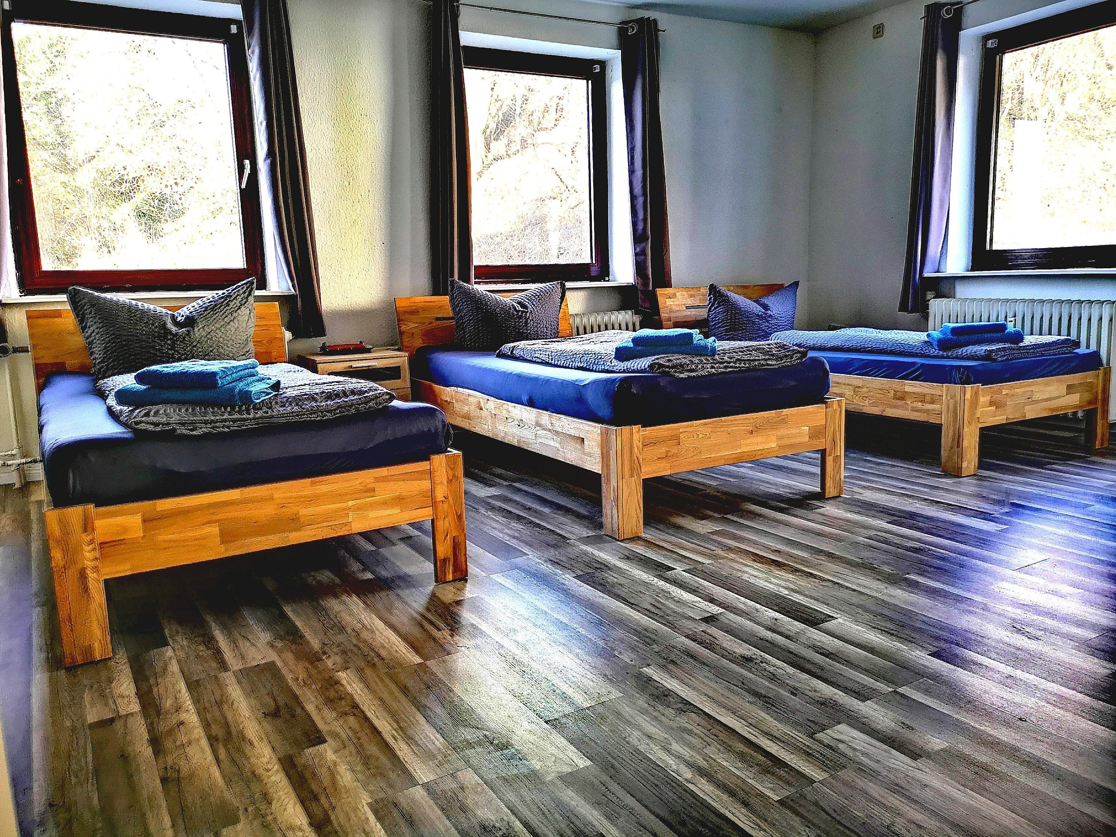 A room with three wooden beds, each with blue bedding and pillows, and a large window with curtains.