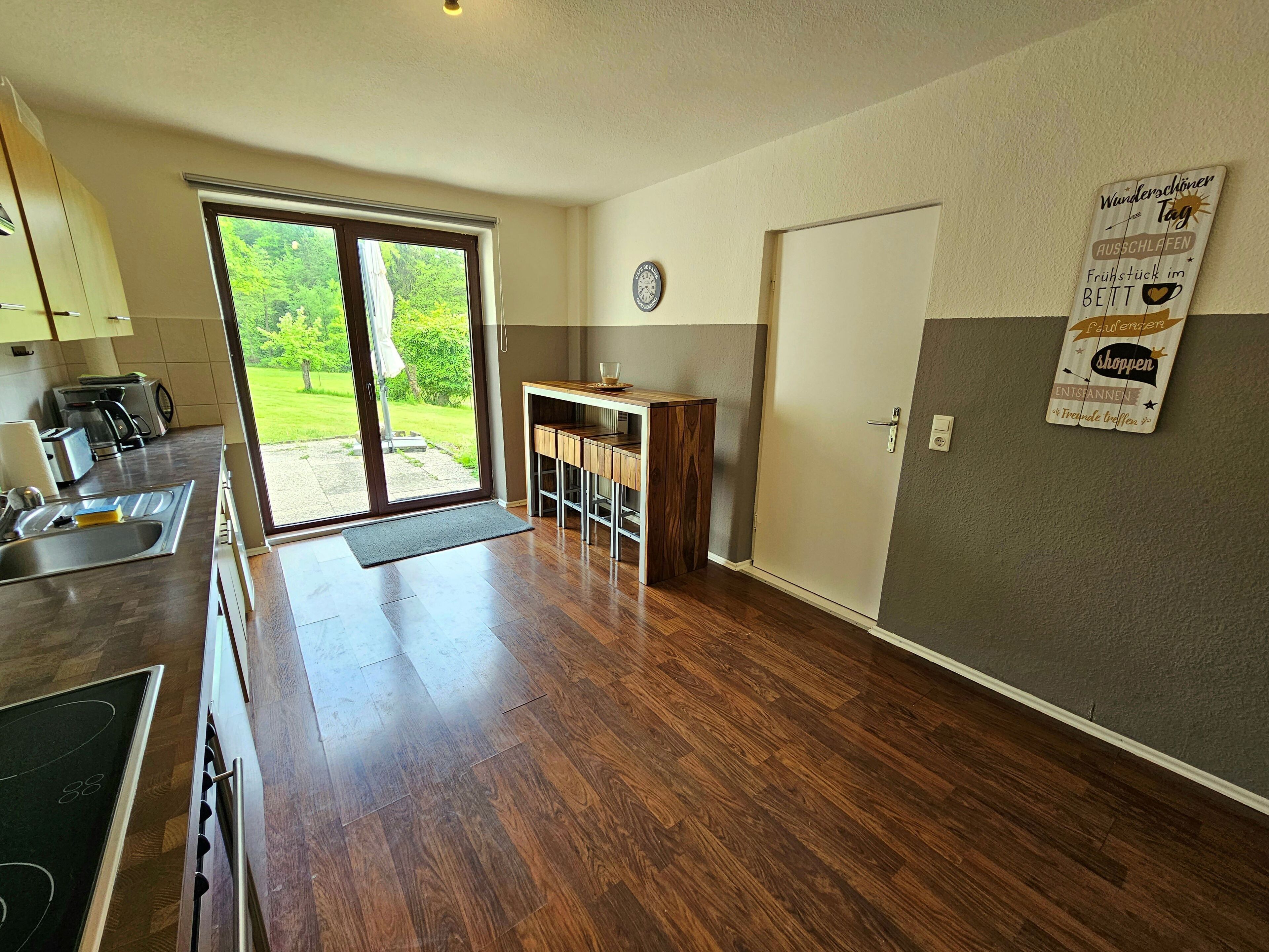 A modern kitchen with a large window, a dining area, and a door leading to a garden.