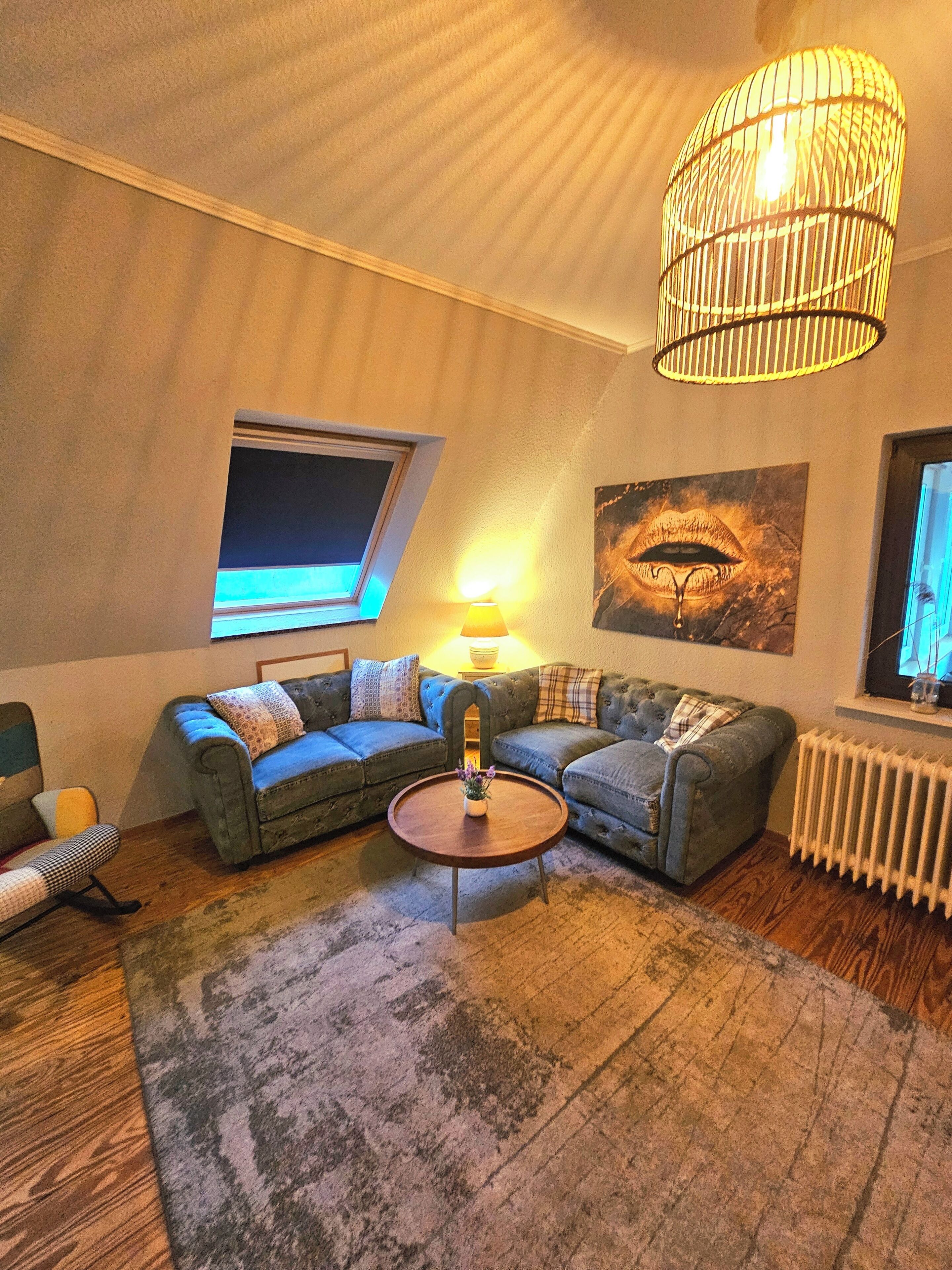 Ein gemütliches Wohnzimmer mit Ecksofa, rundem Couchtisch, großem Fenster und Deckenleuchte.