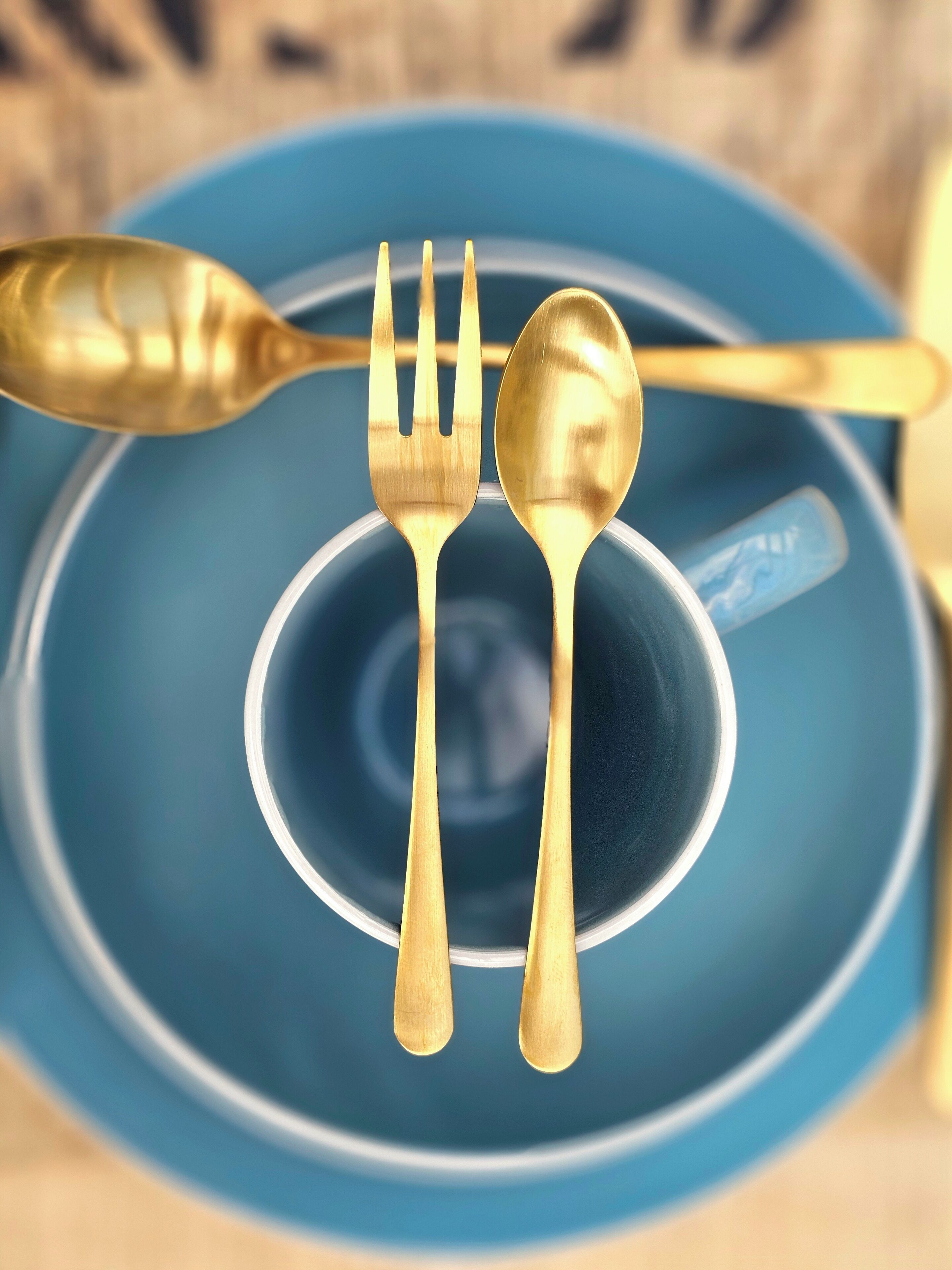 A blue plate with a gold spoon and fork on top.
