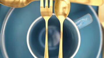 A blue plate with a gold spoon and fork on top.