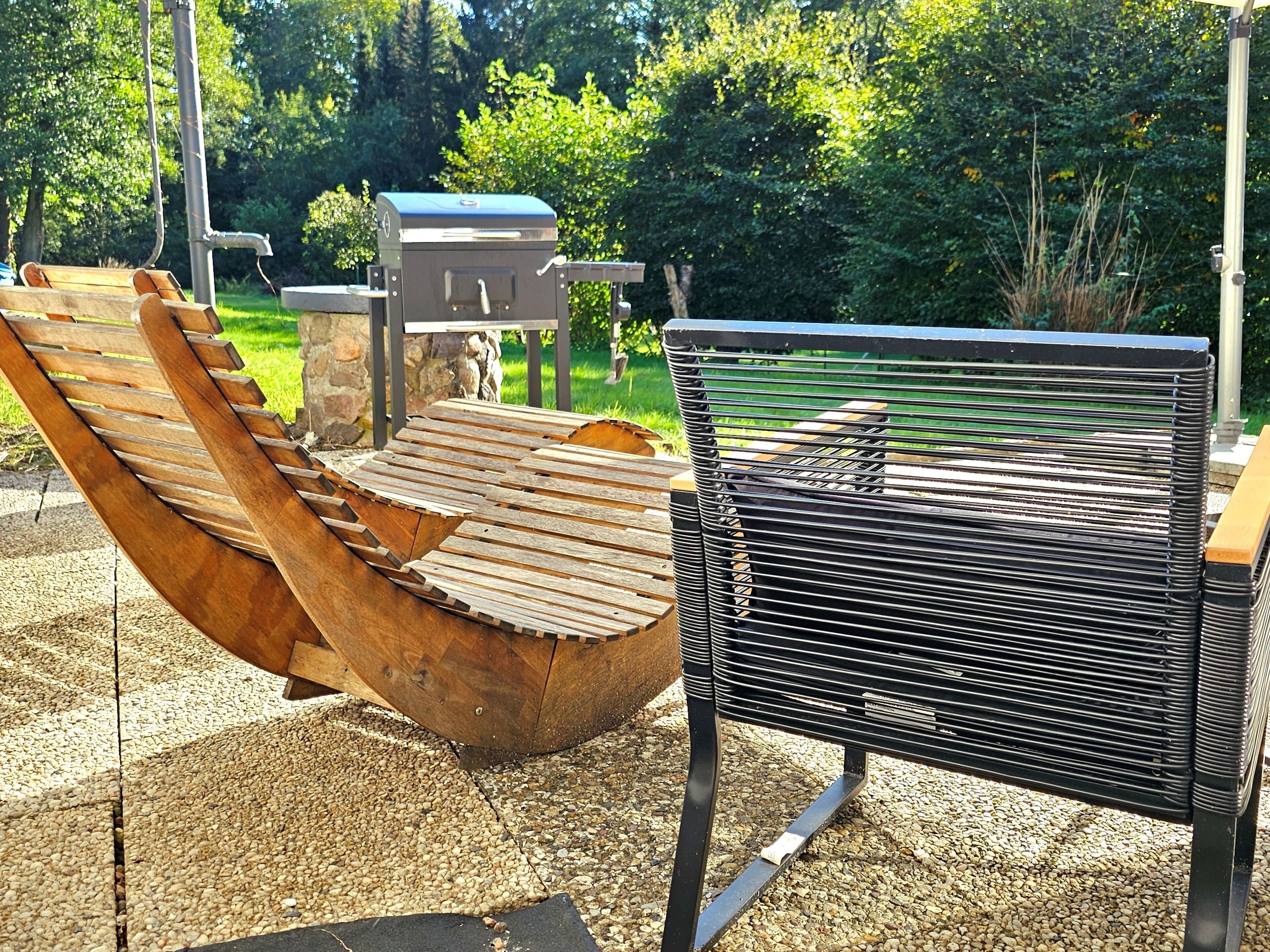 Una cadira de relax de fusta i una barbacoa en un ambient exterior.