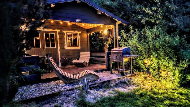 En stuga av trä med en veranda, en grill och ljusslingor.
