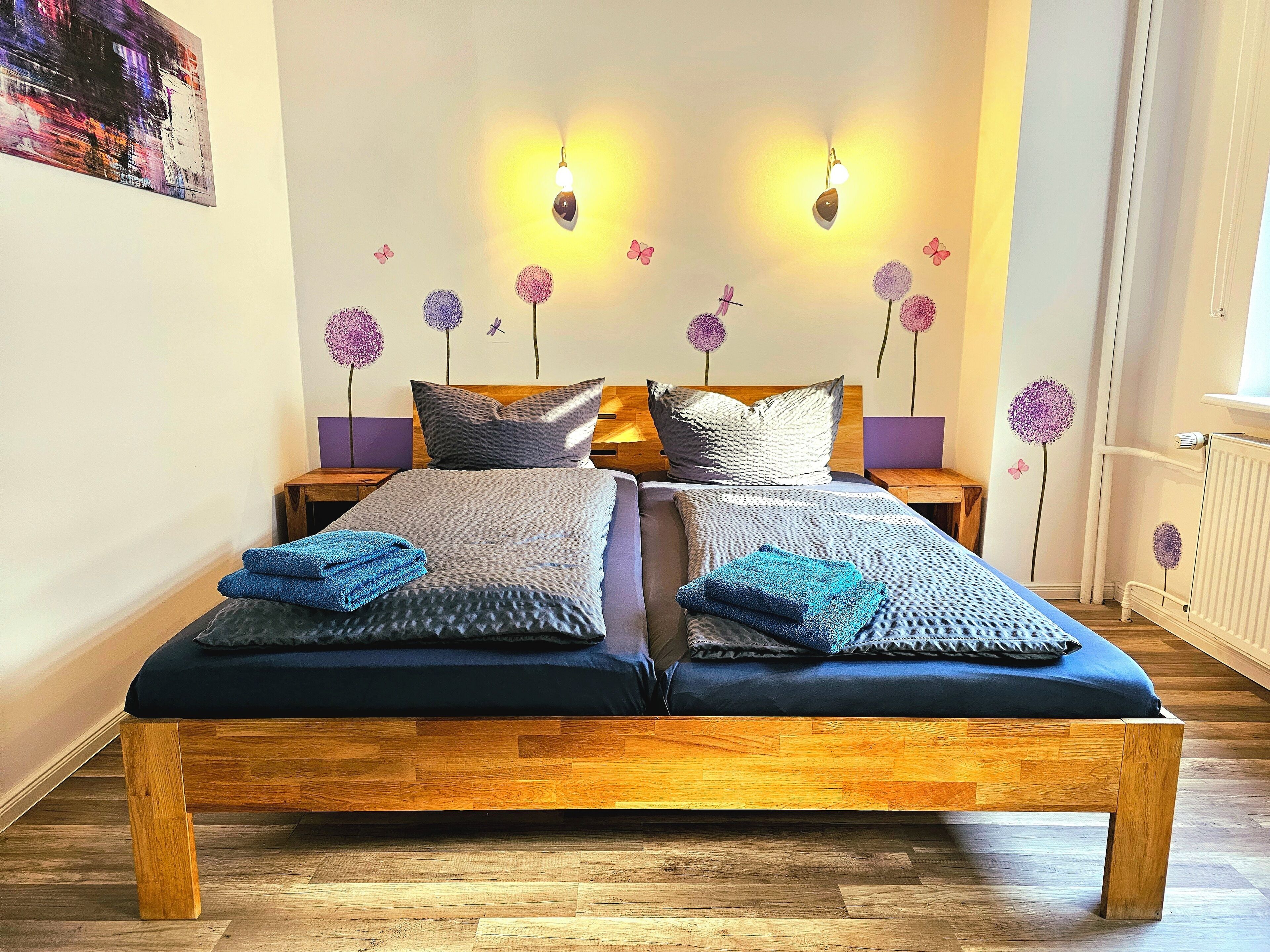 Una cama doble con estructura de madera, dos mesitas de noche y luces fijadas a la pared.