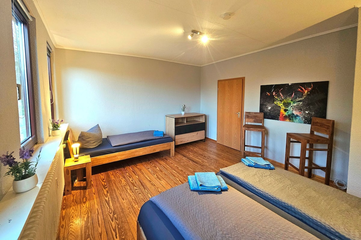Ein kleines Zimmer mit einem Bett, einem Schreibtisch, einem Stuhl, einem kleinen Tisch und einem Bild an der Wand.