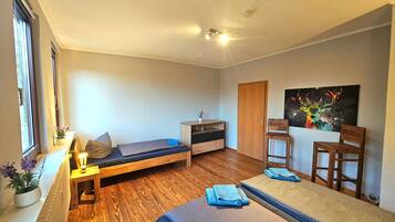 Una habitación pequeña con cama, escritorio, silla, mesita y un cuadro en la pared.