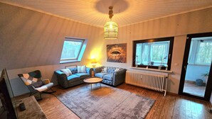 Ett mysigt vardagsrum med en soffa, fåtöljer, ett soffbord och ett element. Det finns fönster och en taklampa.