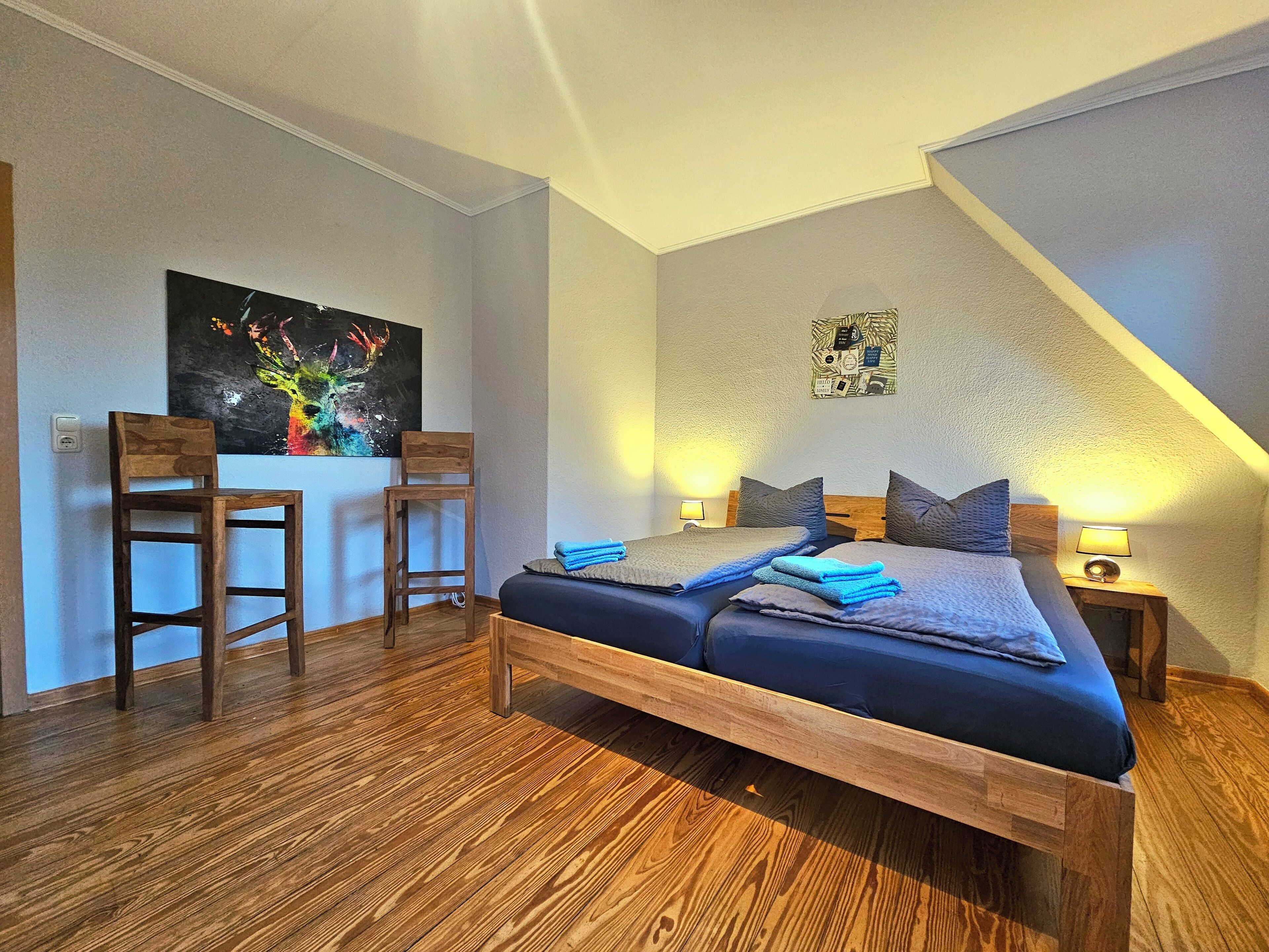 Een slaapkamer met een bed, twee houten stoelen, een schilderij, een kleine tafel met een lamp en een wandklok.