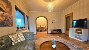 Ett vardagsrum med en soffa, ett soffbord med en växt, en tv på ett skåp och en välvd dörröppning som leder till ett annat rum.