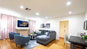 A modern living room with a grey sofa, blue armchairs, a small coffee table, and a TV mounted on the wall. - Family friendly home by Disneyland Universal DTLA SGV Pasadena Arcadia (San Gabriel)
