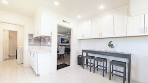 A modern kitchen with white cabinets, a grey countertop, and a TV in the background. - Family friendly home by Disneyland Universal DTLA SGV Pasadena Arcadia (San Gabriel)