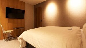 Ein Schlafzimmer mit einem Bett, einem an der Wand befestigten Fernseher, einem Sessel und einer Tür.