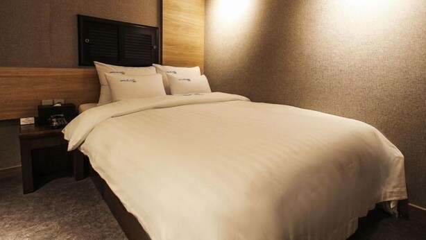 A hotel room with a bed, a nightstand, and a wall-mounted headboard.