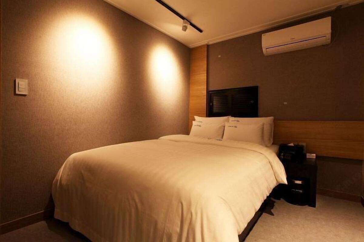 A hotel room with a bed, bedside table, and an air conditioning unit.