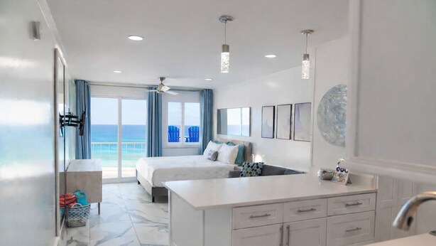 Quarto de hotel moderno com uma cama grande, área de estar, cozinha e vista para o oceano.
