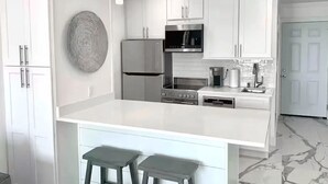 Cozinha moderna com armários brancos, eletrodomésticos de aço inoxidável e painel de fundo de mármore.