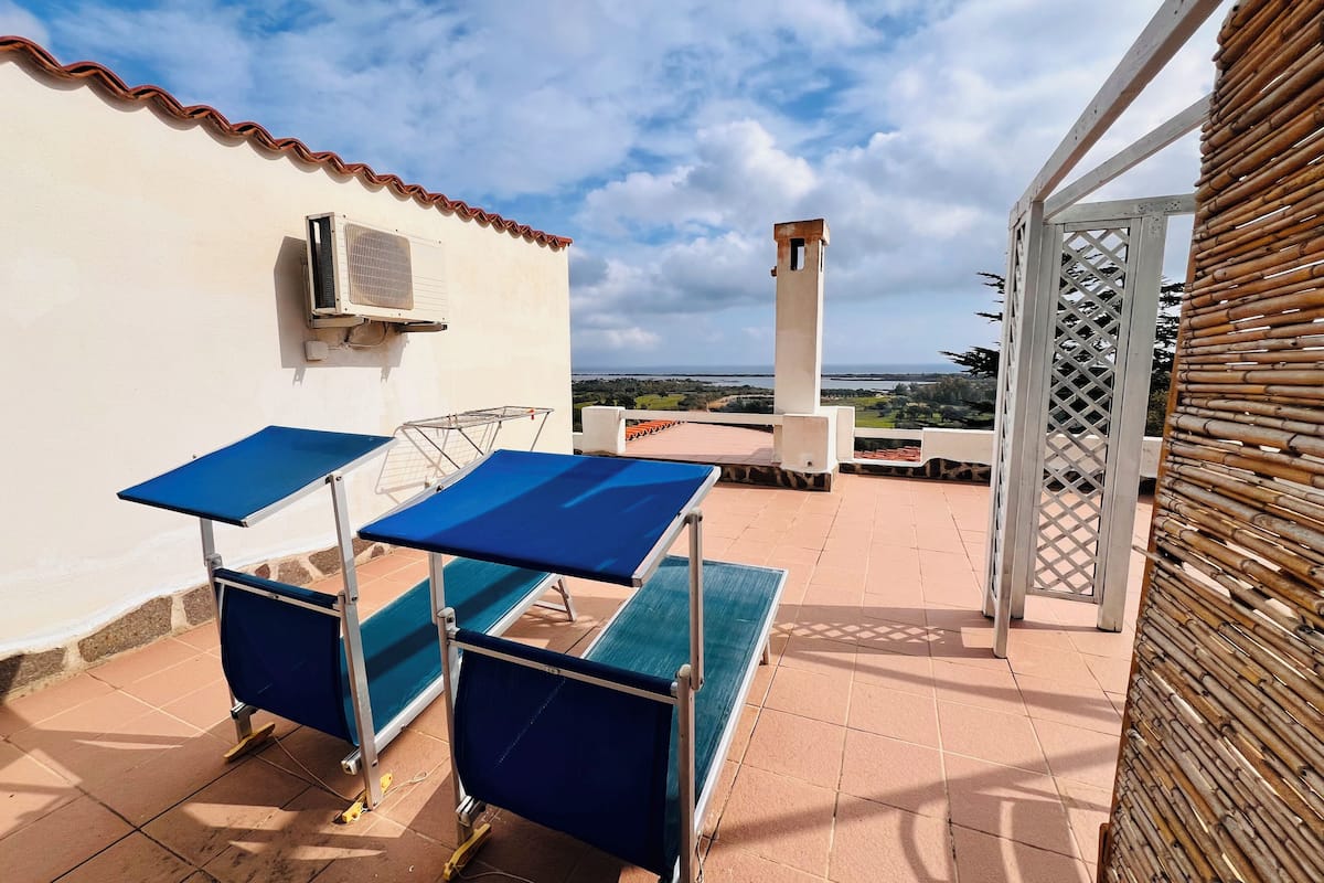 A terrace with two blue tables, a white air conditioning unit, and a view of the landscape.