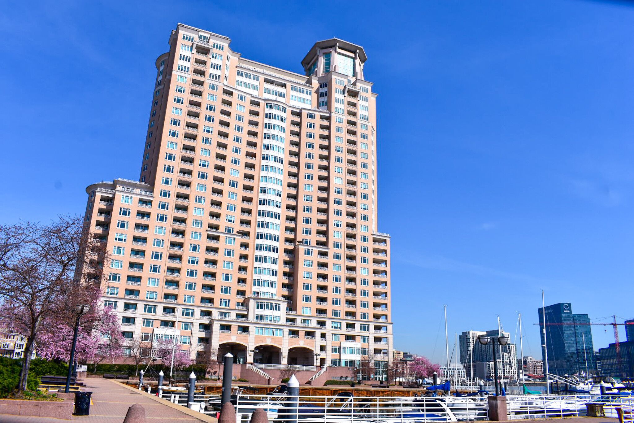 A tall, multi-story building with numerous windows and balconies, situated near a marina with boats.
