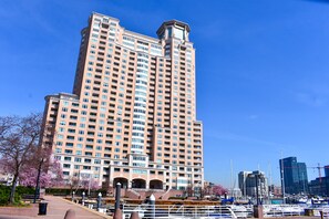 Un grand immeuble à étages, doté de nombreuses fenêtres et de balcons, situé près d’un port de plaisance où sont amarrés des bateaux.