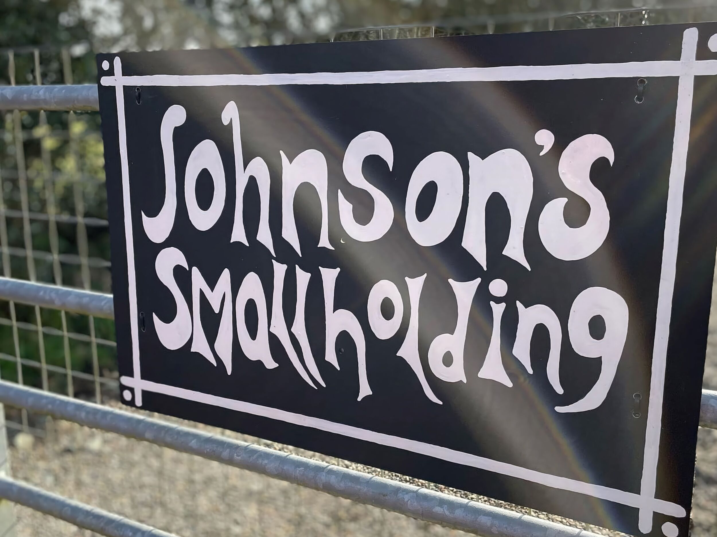 A sign with the text "Johnson's Smullholding" on a black background with white lettering.