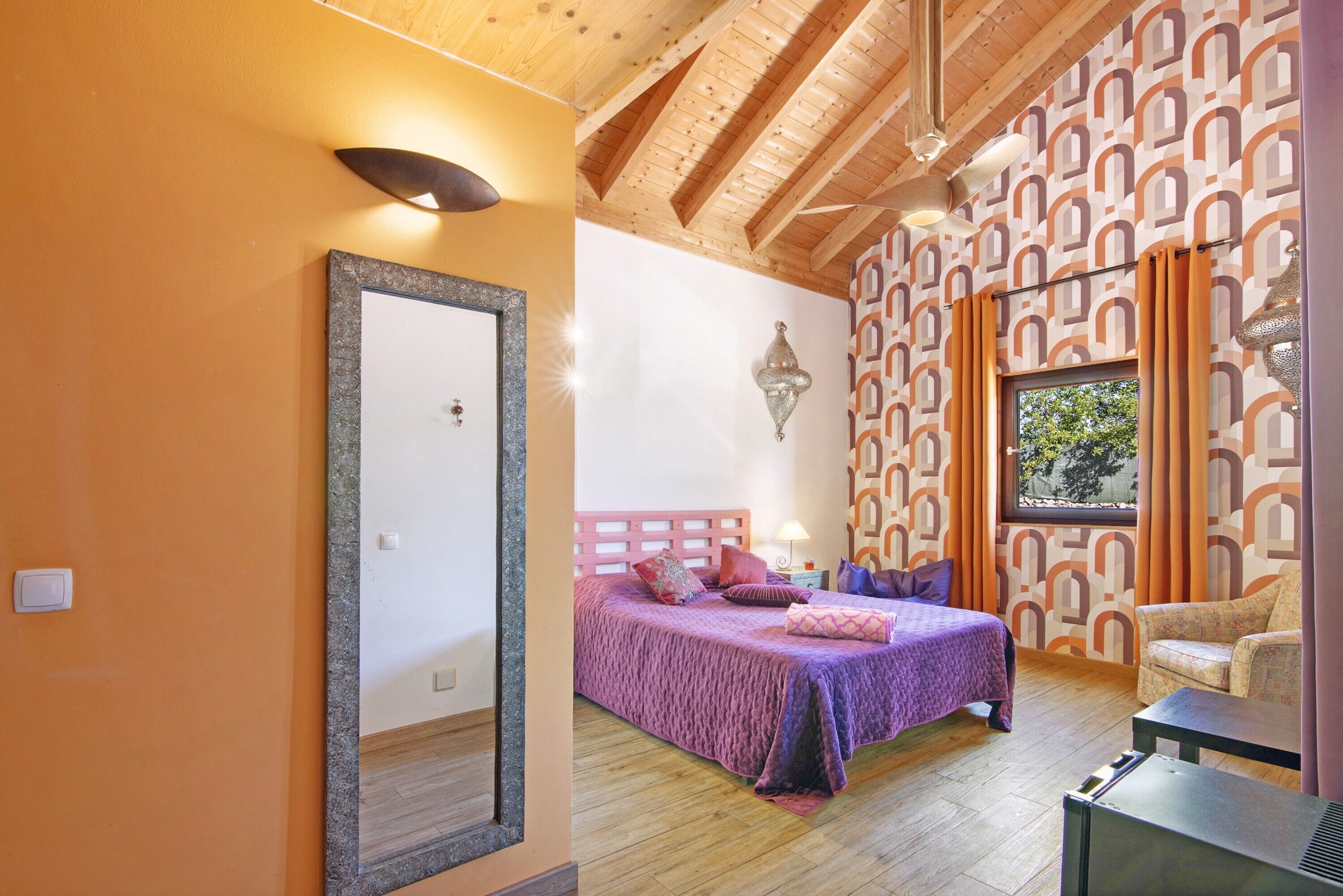 A bedroom with a bed, a chair, a mirror, and a window with curtains.