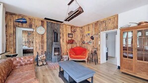 Una sala rústica con pared de madera, una chimenea, un sofá de cuero, un sillón rojo y un aparador de madera.