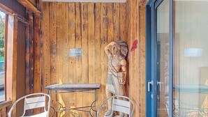 Un interior de madera con una mesa metálica y dos sillas, una estatua de madera y una puerta de vidrio.