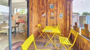 Interior de madera con una mesa y sillas, una puerta de vidrio que da al exterior y varios adhesivos en la pared.