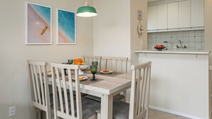 A dining area with a wooden table and chairs, a hanging pendant light, and two framed pictures on the wall.