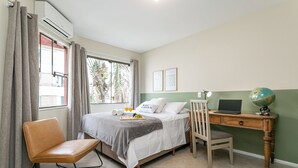 A bedroom with a bed, a desk with a laptop and a globe, a chair, and a window with curtains.