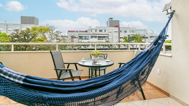 A hammock on a balcony with a table and chairs, overlooking a cityscape.