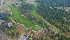 Vista aérea de un campo de golf con un camino sinuoso, zonas residenciales y bosques densos.