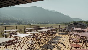 An outdoor terrace with tables and chairs, overlooking a mountainous landscape.
