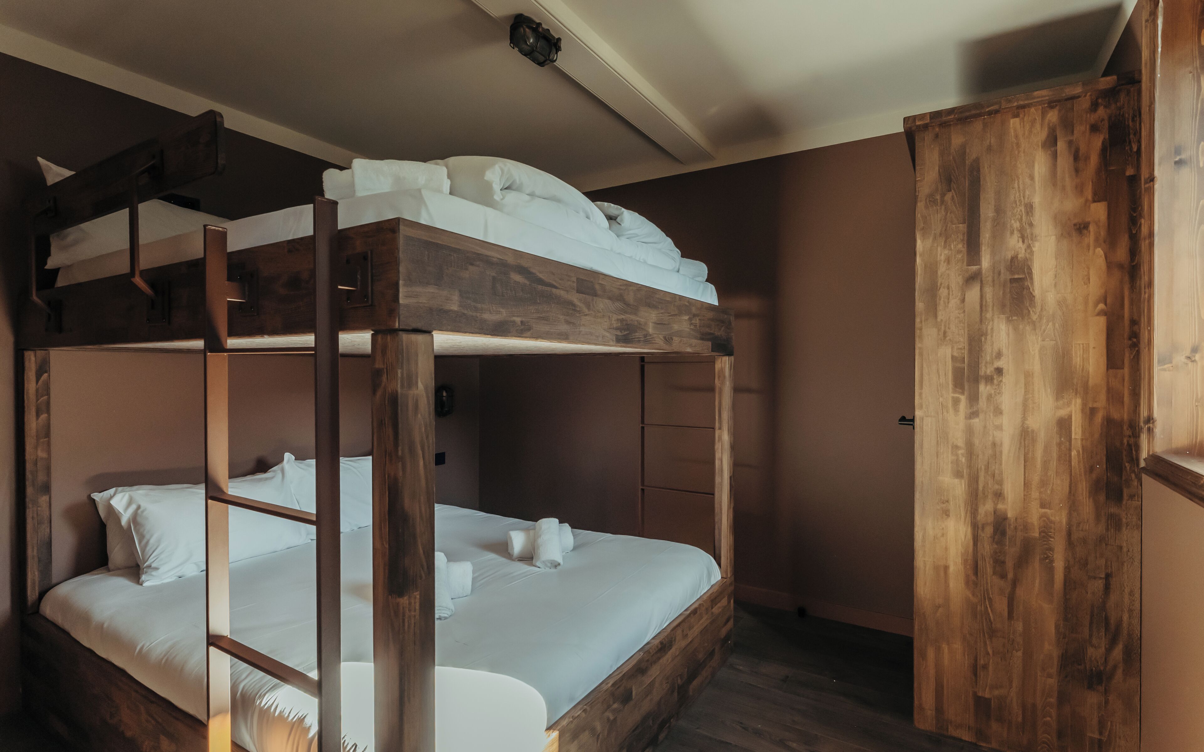 A bunk bed with white bedding, a wooden headboard, and a wooden wardrobe.