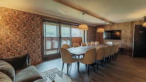 A dining area with a large table, chairs, a sofa, and a TV on the wall.